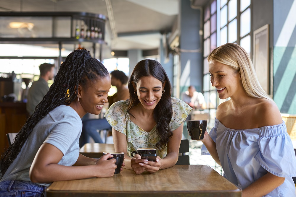 Group Of Female Friends Meeting Up In Restaurant Or Coffee Shop Looking At Mobile Phone Atlanta cafe