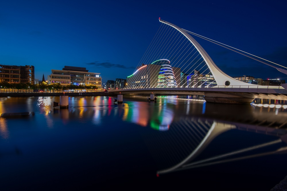 a bridge that is over the water at night time and with lights reflecting in it Samuel Beckett bridge in Dublin Ireland