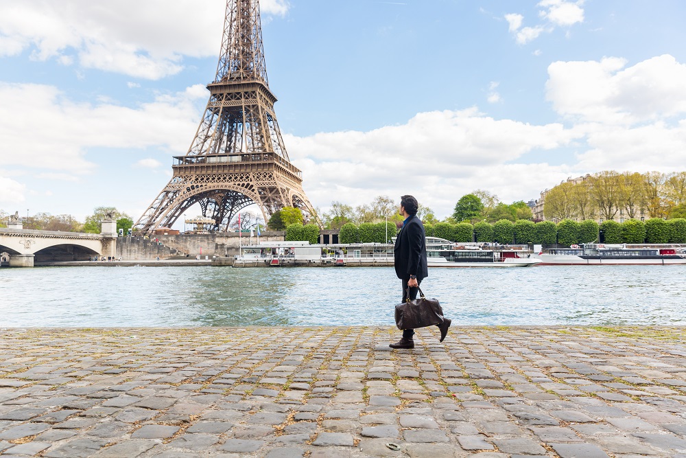 Businessman using smartphone while leaning on bridge in city Businessman walking along the river in front of Eiffel Tower