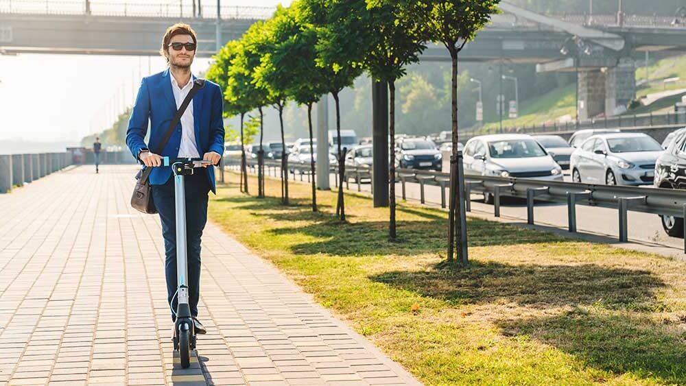 Young businessman riding electric scooter on road in city while there traffic. Bleisure travel business traveler in the city on scooter