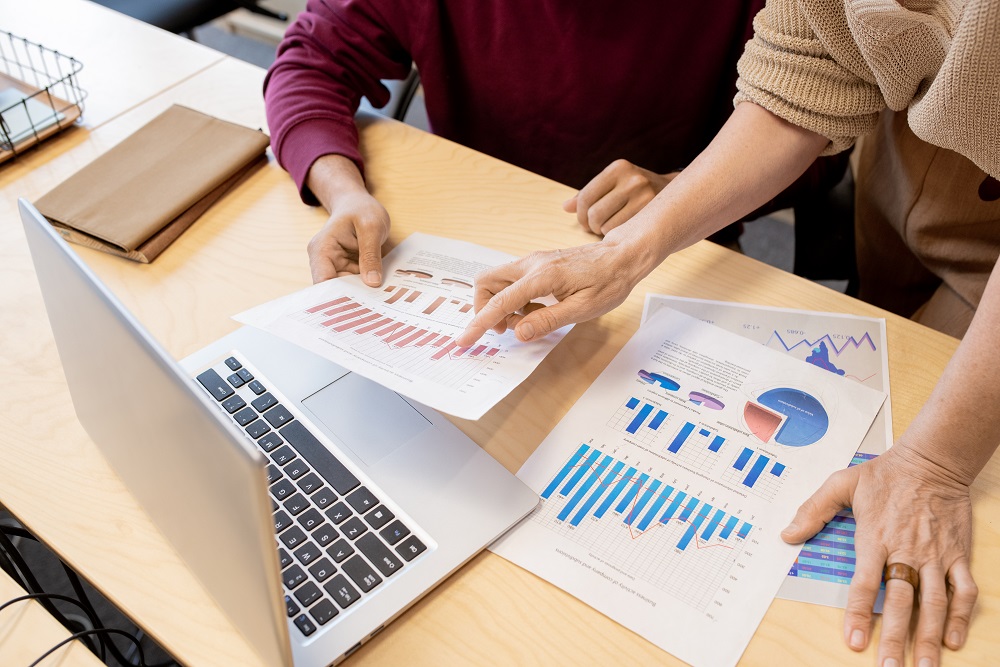 Hands of contemporary mature female broker pointing at one of financial papers Zwei Personen, die gemeinsam eine Finanzanalyse durchführen