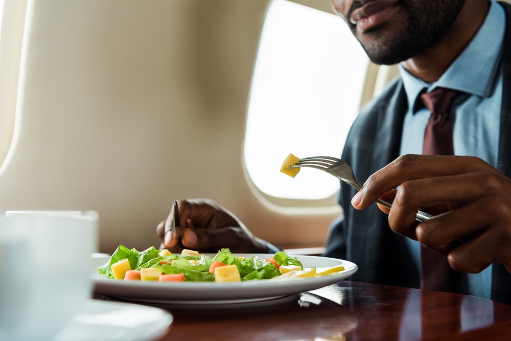 cropped view of african american man eating salad in private plane Geschäftsreisender isst einen Salat in der Business Class eines Flugzeugs