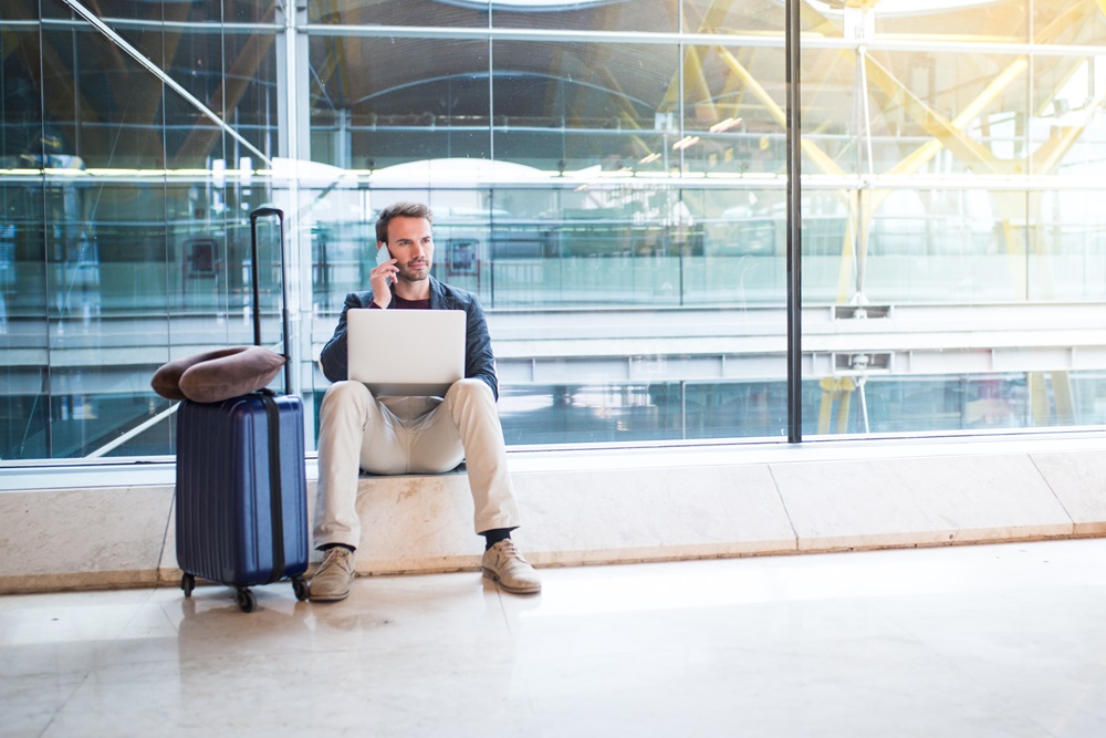 man sitting at the airport using laptop and mobile phone next to Geschäftsreisender nutzt Laptop und telefoniert während eines Zwischenstopps mit dem Handy