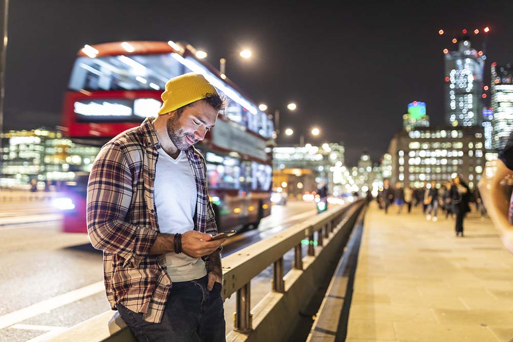 UK, London, smiling man using phone at the street in the city at night jet lag tips
