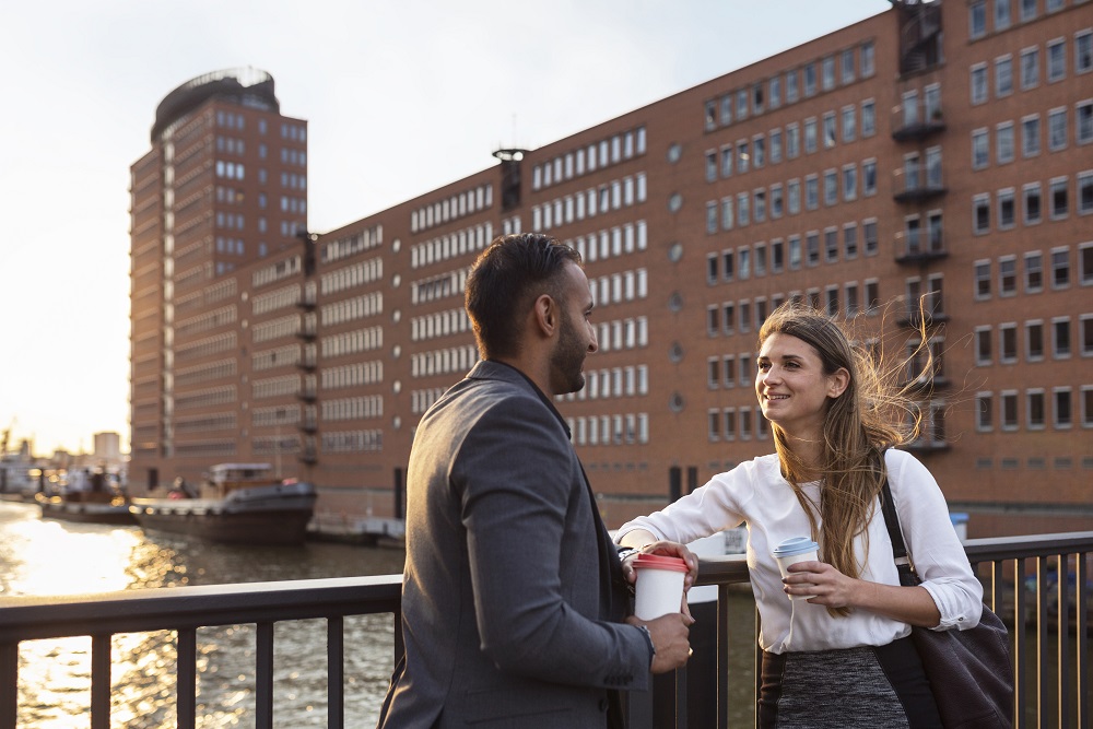Man and woman talking on bridge and holding coffee cups Zwei Kollegen auf einer Brücke mit Kaffeetassen in den Händen