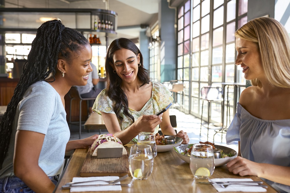 Group Of Female Friends Meeting Up In Restaurant Or Coffee Shop Looking At Mobile Phone Café in Atlanta