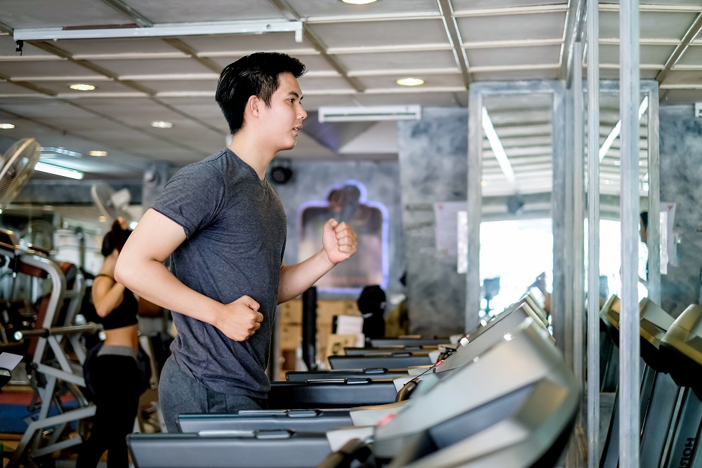 Asian man running in machine treadmill at gym. Side view running to improve mental health