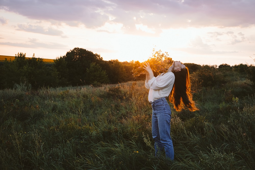 National Relaxation Day, relaxation practices, mental health, slow living concept. Young girl with long windy hair and flower bouquet enjoying nature on the background of sunset how to improve mental health