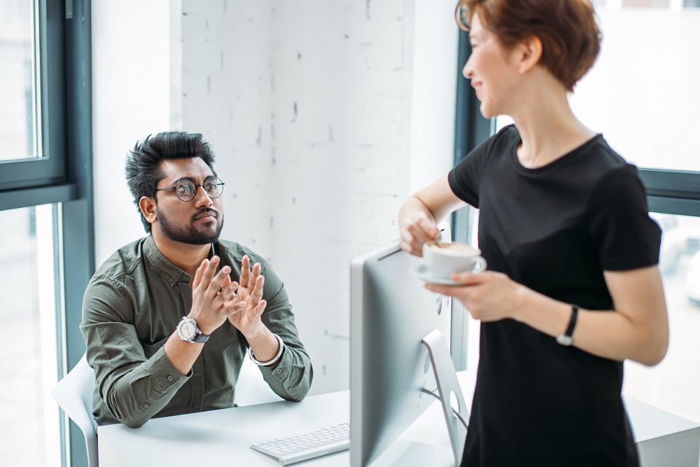 mentor boss smiling looking at young male coworker and drink coffee, teaching helping colleague Angestellter, der locker mit dem Chef in einem Büroumfeld spricht