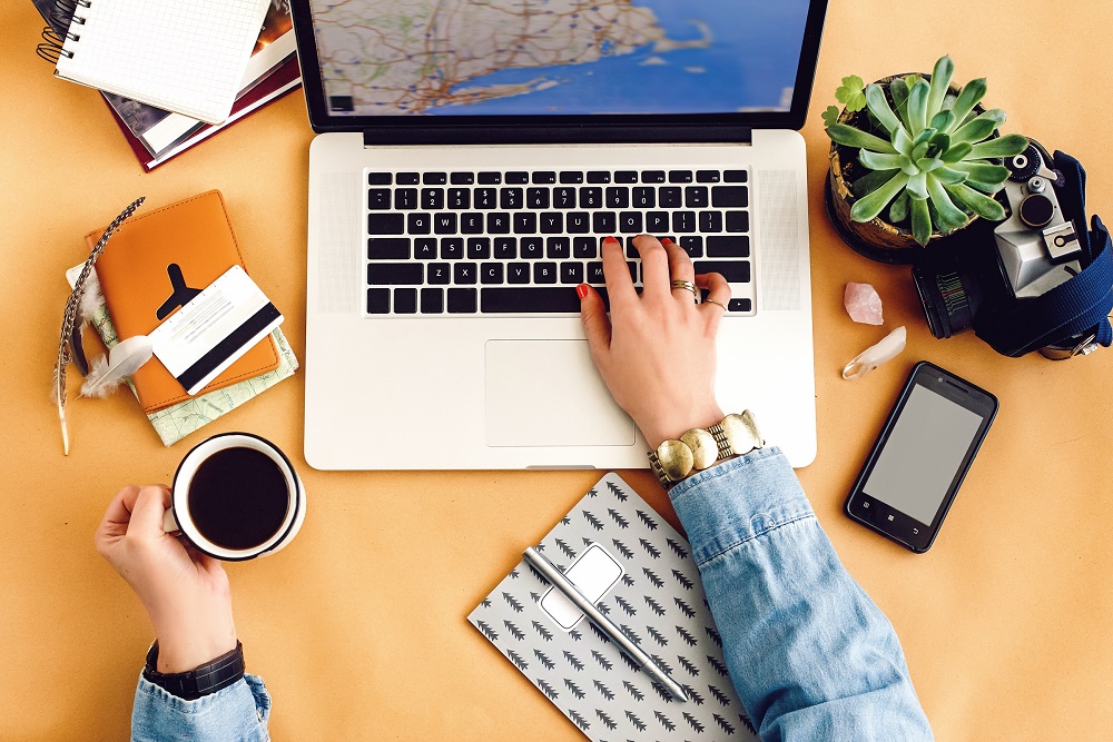 Frau, die das Online-Buchungstool von ihrem Laptop aus benutzt, mit einer Kaffeetasse und einem Handy auf dem Schreibtisch