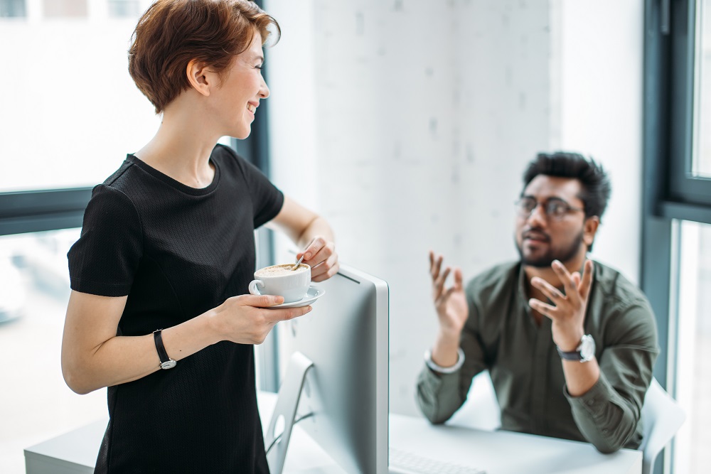 mentor boss smiling looking at young male coworker and drink coffee, teaching helping colleague Employee having an informal chat with boss with coffee cup in hands