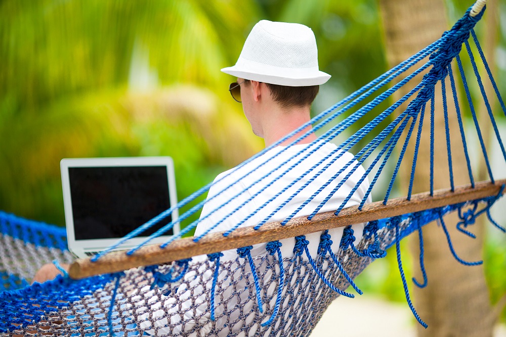 Young man with laptop at hammock on tropical vacation Remote-Arbeiter, der eine Videokonferenz aus der Hängematte führt