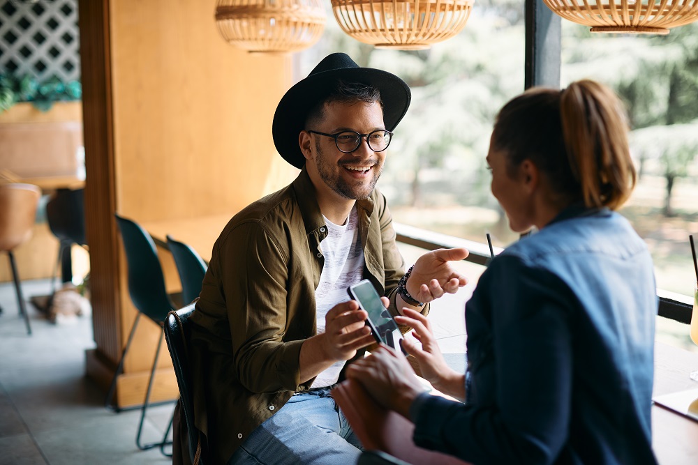 Young happy couple having fun while using mobile phone in a cafe. what is a travel management company