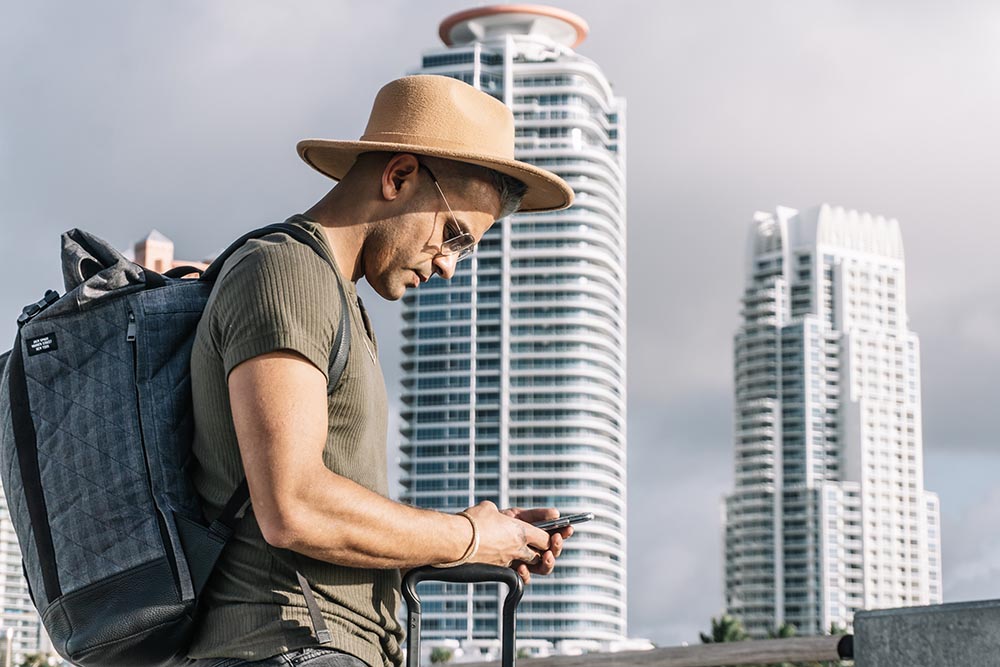 Close up, profile of traveller man with a brown hat, looking for direction on his smartphone. Man on a business trip taking part in corporate travel planning