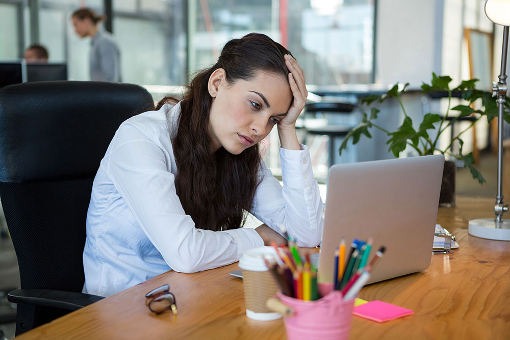 Upset female business executive looking at laptop in office Girl at office looking at computer with head resting in hand