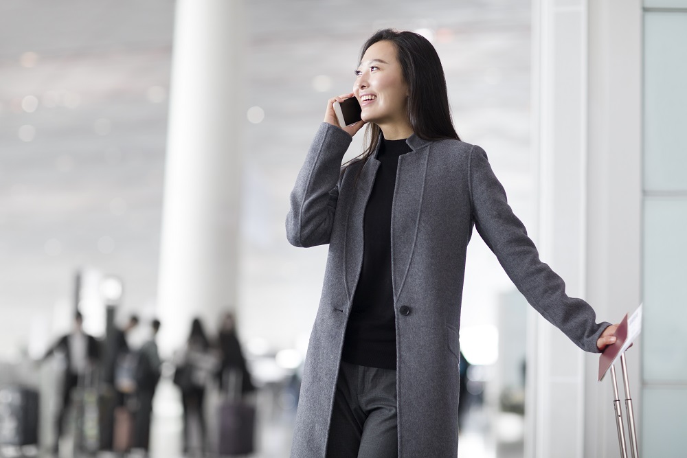 Chinese businesswoman talking on cell phone at the airport functions of a travel management company